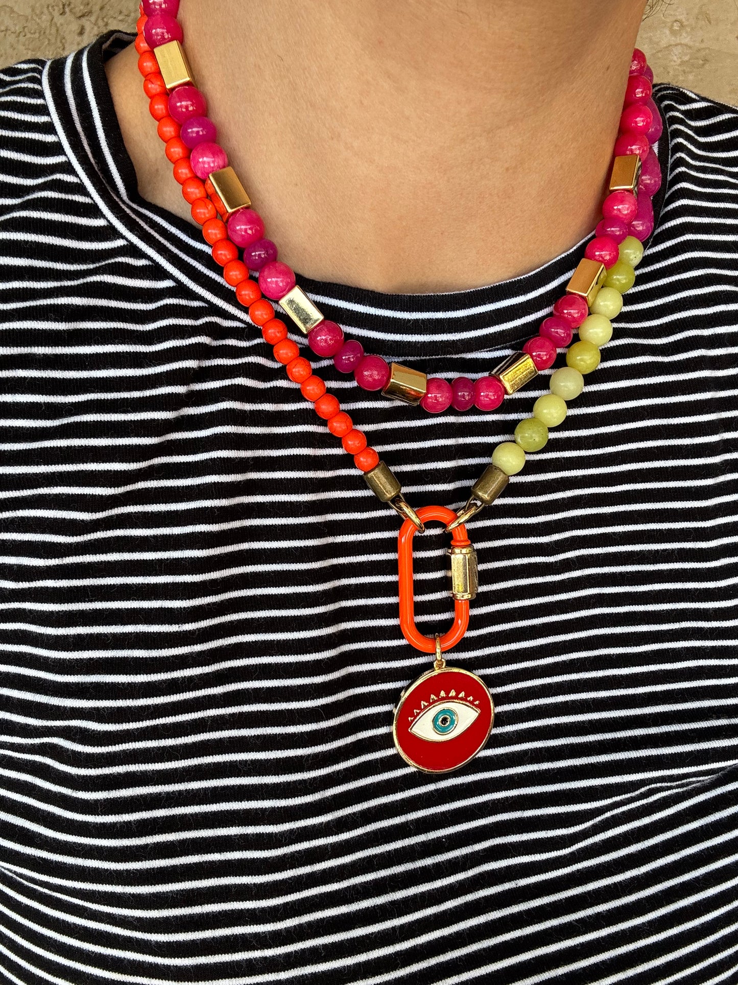 Colorful beaded lanyard with a red eye charm attached to a striped shirt.