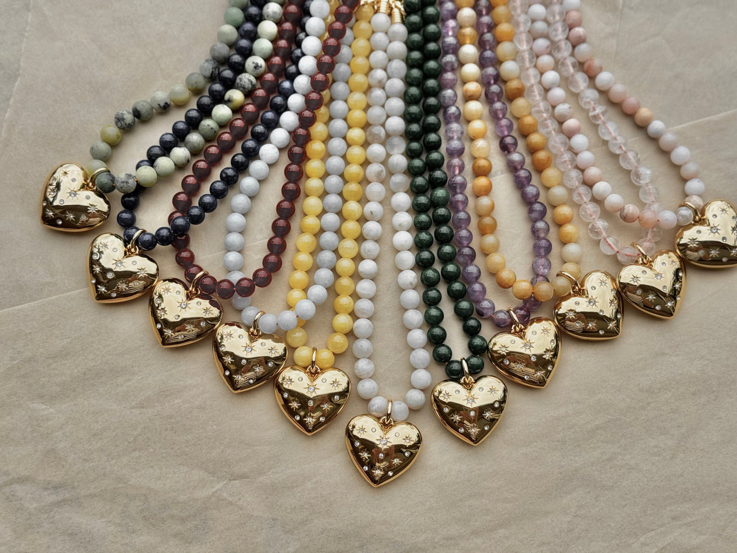 Set of beaded necklaces with gold heart pendants on a textured surface