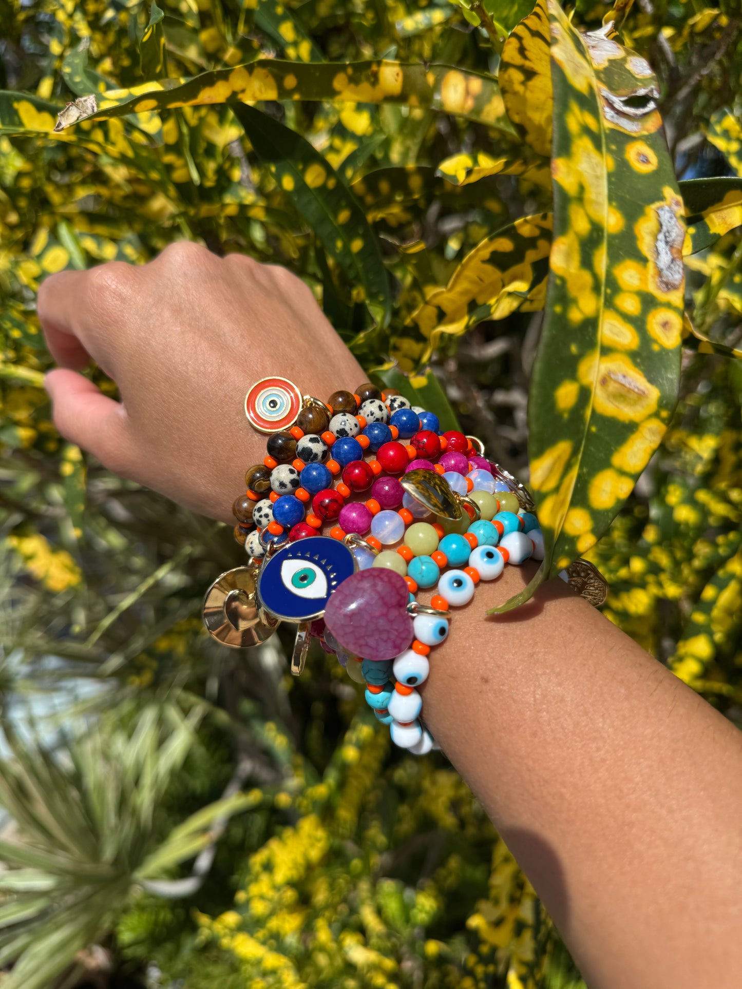 Colorful beaded bracelets on a wrist with a green leafy background