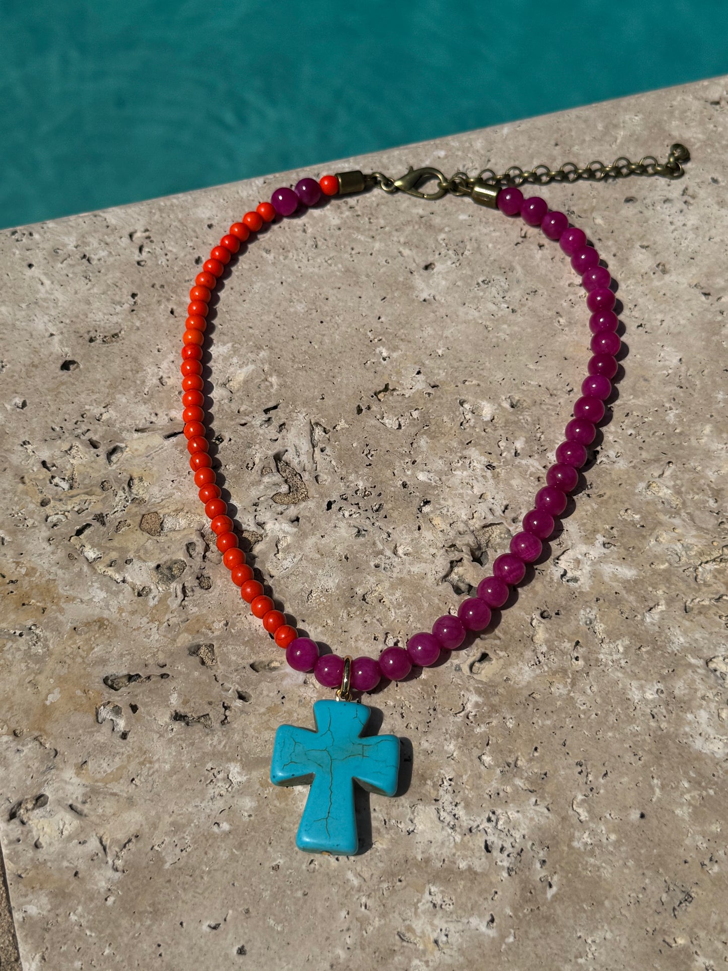 Necklace with red, pink, and turquoise beads on a stone surface with water in the background