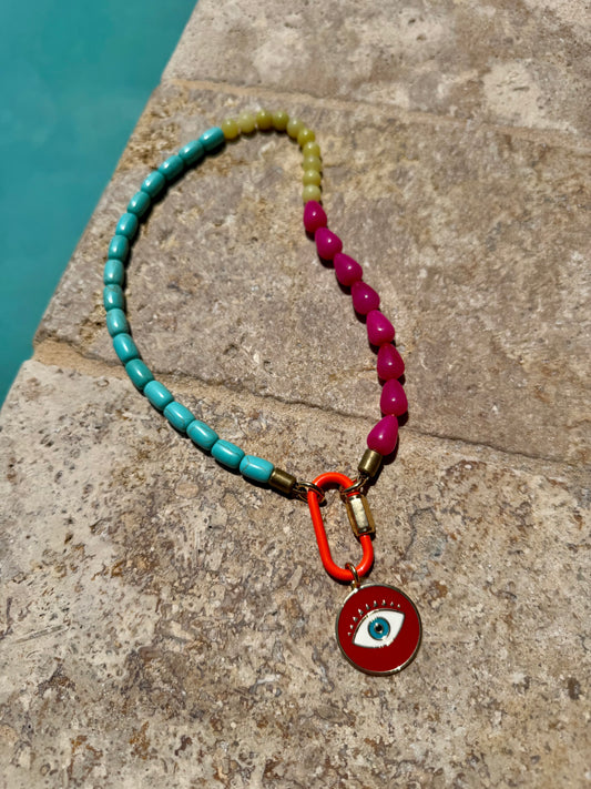 Necklace with colorful beads and a red pendant on a stone surface near water.
