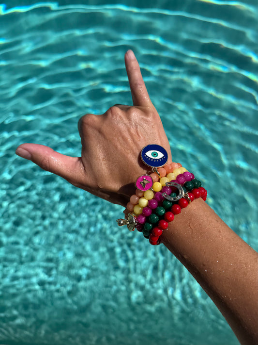 Hand with colorful bracelets making a peace sign in front of a pool.