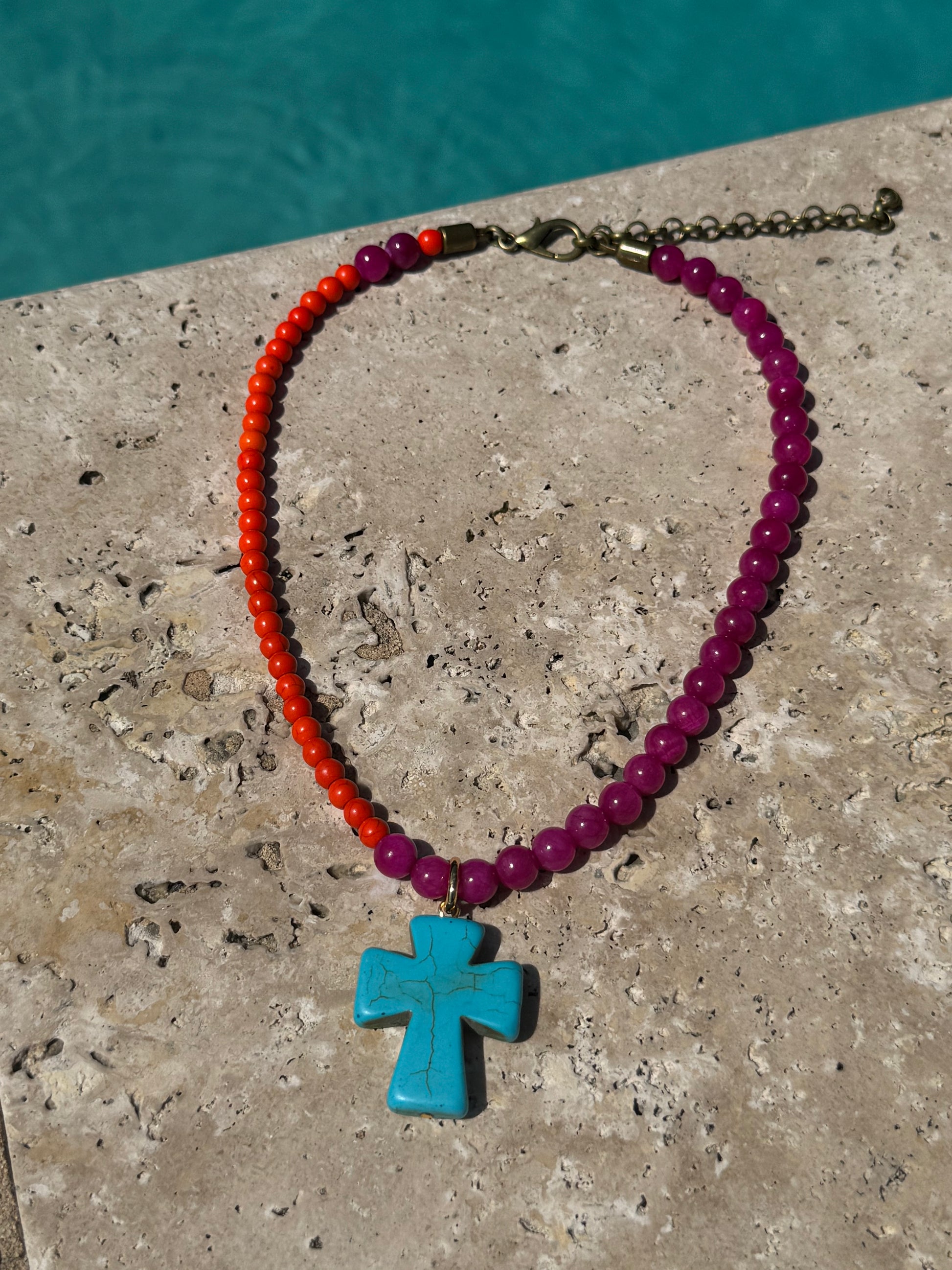 Necklace with red, pink, and turquoise beads on a stone surface with water in the background