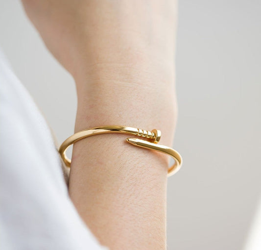 Gold bracelet on a wrist with a plain background